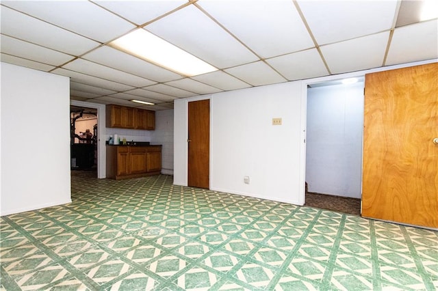 unfurnished living room featuring a drop ceiling, baseboards, and light floors