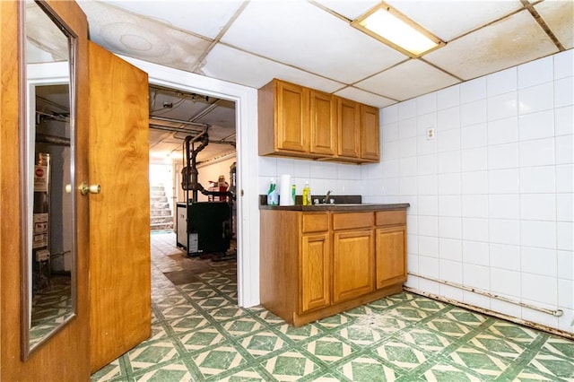 bar with a drop ceiling, light floors, tile walls, and a sink