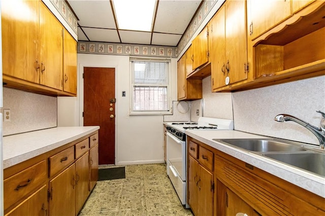 kitchen with gas range gas stove, light countertops, decorative backsplash, brown cabinets, and a sink