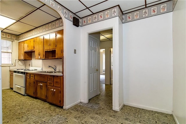 kitchen with a sink, baseboards, gas range gas stove, and light floors