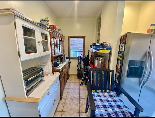 kitchen featuring glass insert cabinets, light countertops, light tile patterned flooring, stainless steel fridge, and white cabinetry