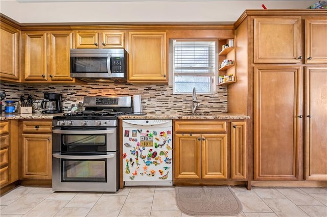 kitchen with a sink, light stone counters, appliances with stainless steel finishes, and brown cabinetry