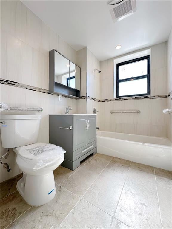 full bathroom with visible vents, toilet, shower / washtub combination, tile walls, and vanity