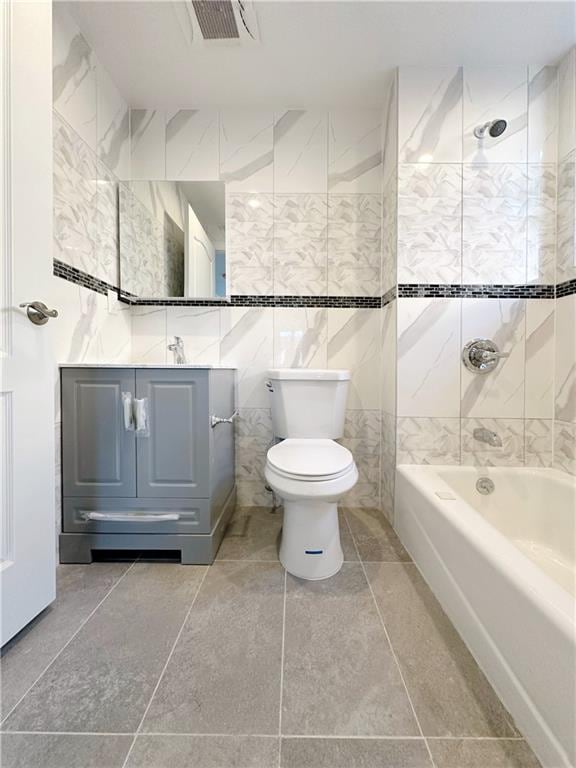 bathroom with visible vents, toilet, vanity, bathing tub / shower combination, and tile walls