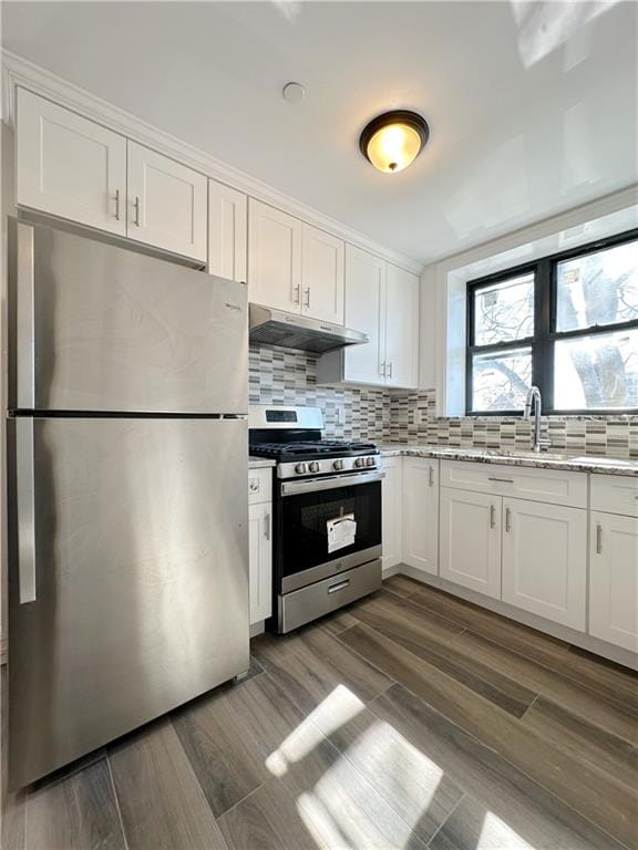 kitchen featuring under cabinet range hood, backsplash, white cabinetry, stainless steel appliances, and light stone countertops