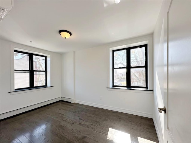 empty room featuring a wealth of natural light, a baseboard heating unit, baseboards, and dark wood-type flooring