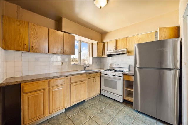 kitchen featuring freestanding refrigerator, a sink, decorative backsplash, white gas range oven, and under cabinet range hood