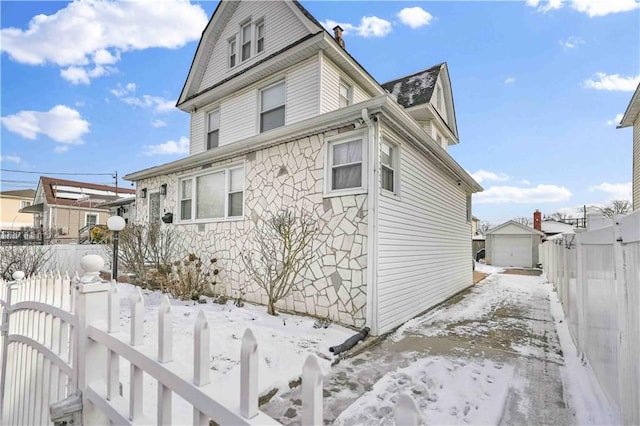 snow covered property featuring a gate, fence, a chimney, an outdoor structure, and a garage