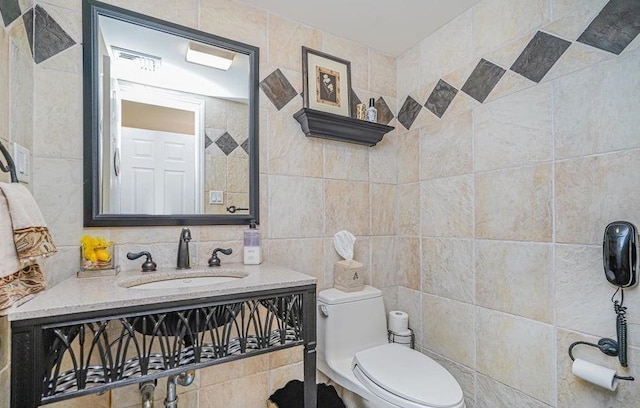 half bathroom with tile walls, toilet, visible vents, and a sink