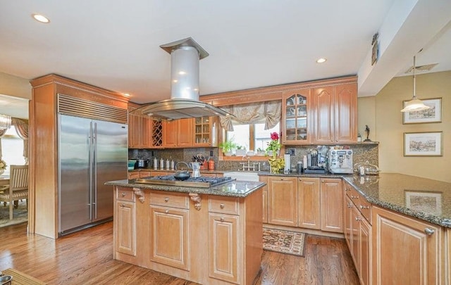 kitchen featuring island exhaust hood, appliances with stainless steel finishes, wood finished floors, and dark stone countertops