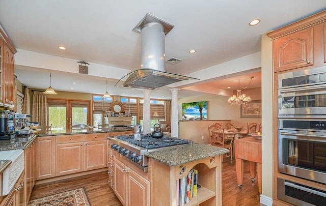 kitchen featuring dark stone counters, decorative columns, appliances with stainless steel finishes, wood finished floors, and a warming drawer