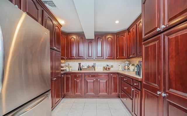 kitchen with light tile patterned floors, light countertops, freestanding refrigerator, and reddish brown cabinets