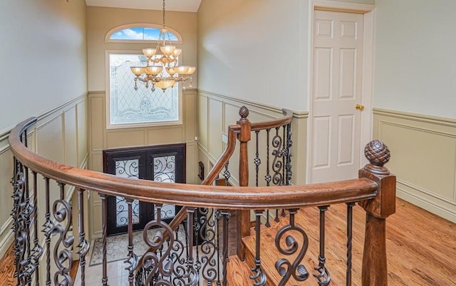 stairs featuring a wainscoted wall, an inviting chandelier, and wood finished floors