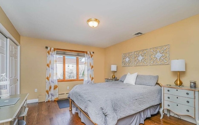 bedroom featuring visible vents, baseboards, baseboard heating, and wood finished floors