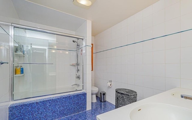 bathroom with double vanity, a sink, tiled shower / bath combo, tile walls, and toilet