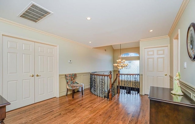 living area featuring wood finished floors, a wainscoted wall, visible vents, a notable chandelier, and an upstairs landing