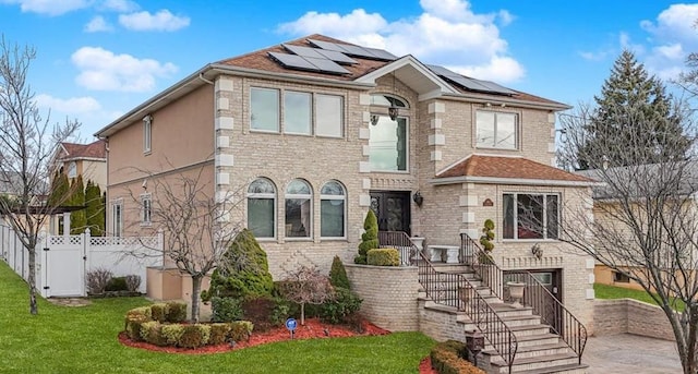 view of front of property featuring stucco siding, a front lawn, a gate, roof mounted solar panels, and fence