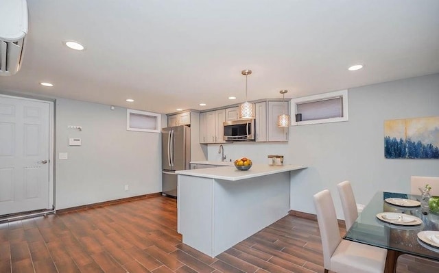 kitchen with dark wood-type flooring, a breakfast bar, light countertops, a peninsula, and stainless steel appliances