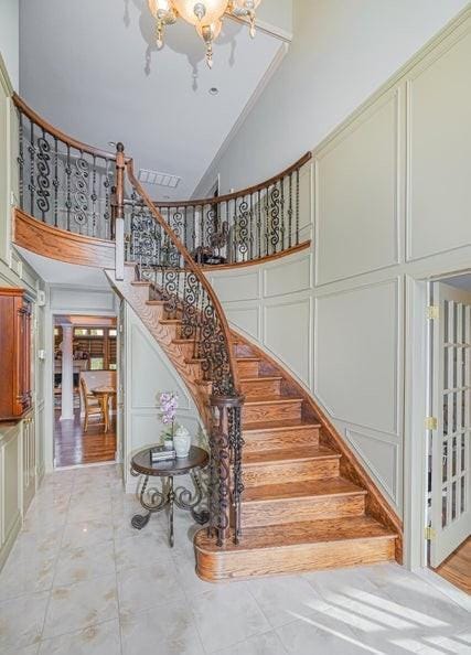 staircase with a notable chandelier, high vaulted ceiling, and a decorative wall