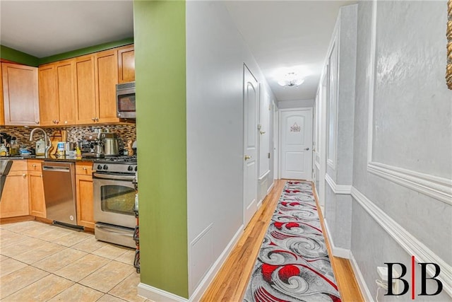 kitchen featuring a sink, tasteful backsplash, dark countertops, appliances with stainless steel finishes, and light wood finished floors