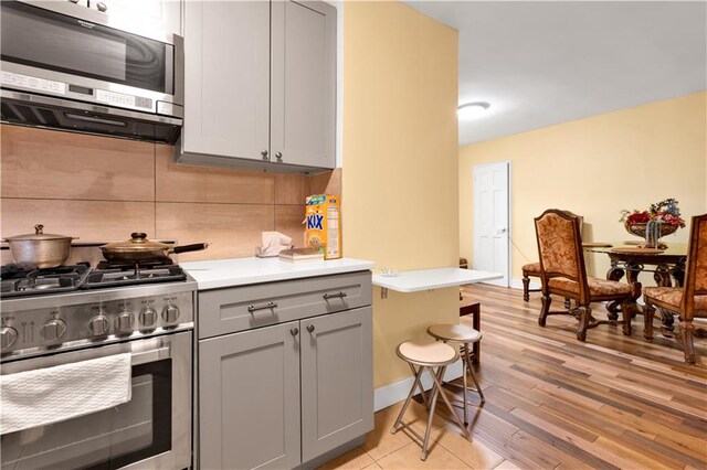 kitchen featuring gray cabinetry, backsplash, light wood-style floors, appliances with stainless steel finishes, and light countertops