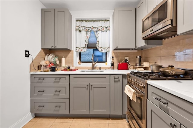 kitchen with gray cabinetry, light countertops, light tile patterned floors, stainless steel appliances, and a sink