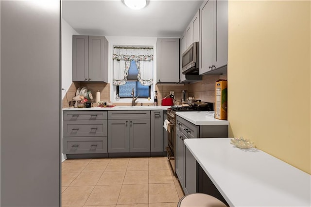 kitchen with gray cabinets, backsplash, stainless steel appliances, light countertops, and light tile patterned floors