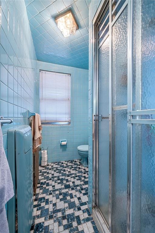 bathroom with tile patterned flooring, tile walls, toilet, and a shower stall