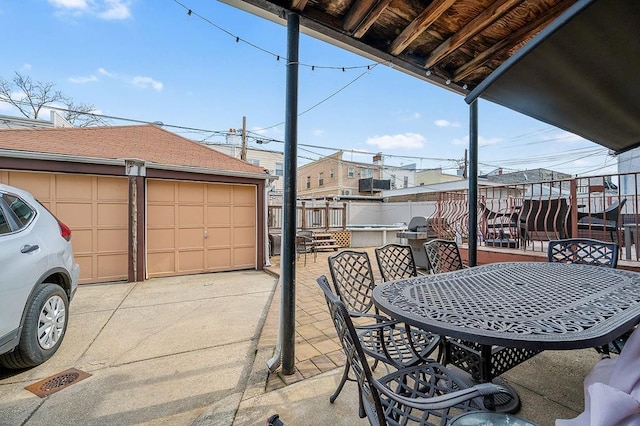 view of patio featuring a garage, an outdoor structure, outdoor dining space, and fence