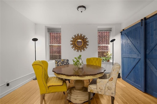 dining space featuring a barn door, baseboards, and light wood finished floors