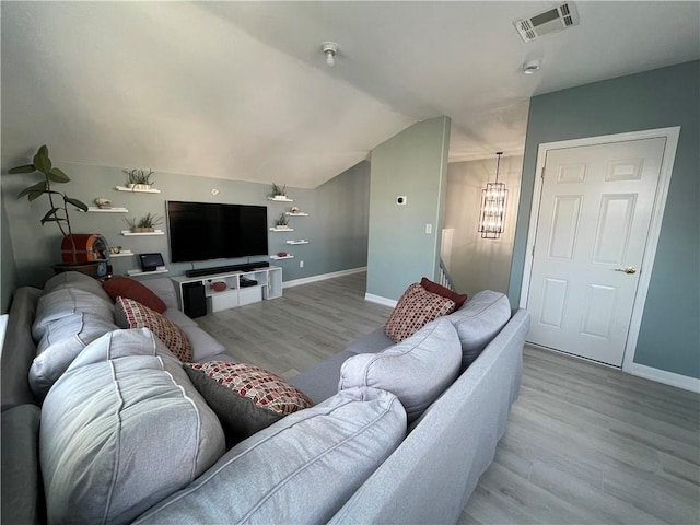 living area with visible vents, lofted ceiling, wood finished floors, an inviting chandelier, and baseboards