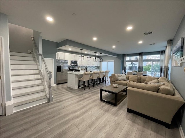 living room featuring recessed lighting, visible vents, light wood-style flooring, and stairway