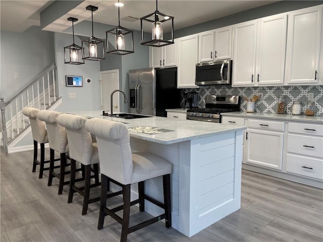 kitchen with light wood finished floors, a sink, white cabinets, appliances with stainless steel finishes, and backsplash