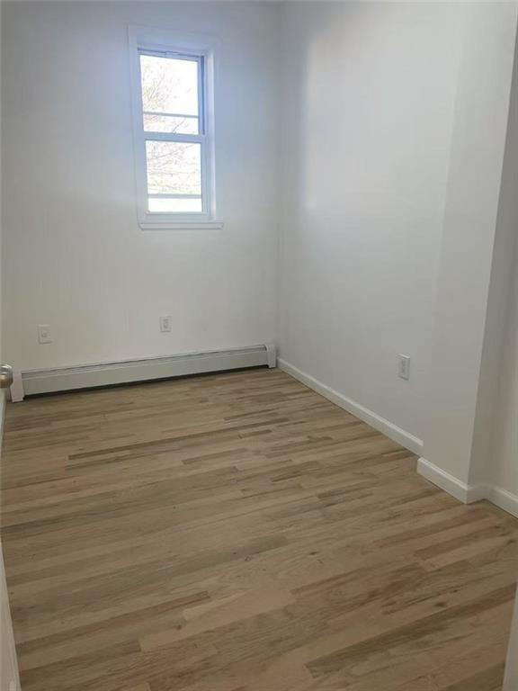 empty room featuring a baseboard heating unit, light wood-style flooring, and baseboards