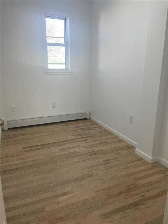 empty room featuring light wood-style flooring, baseboards, and a baseboard radiator