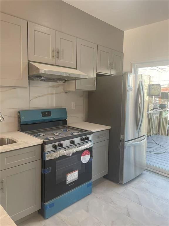 kitchen featuring range with gas stovetop, freestanding refrigerator, gray cabinetry, under cabinet range hood, and marble finish floor