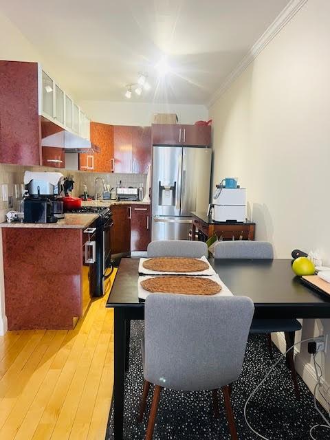 kitchen with light wood-type flooring, ornamental molding, stainless steel refrigerator with ice dispenser, a sink, and tasteful backsplash