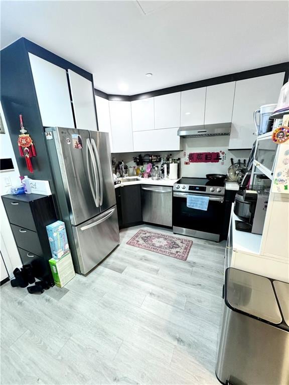 kitchen with under cabinet range hood, light countertops, light wood-style flooring, appliances with stainless steel finishes, and white cabinetry