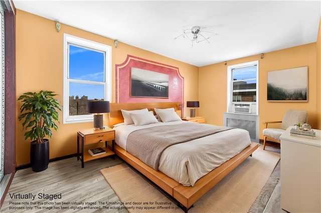 bedroom with cooling unit, baseboards, and light wood-style flooring