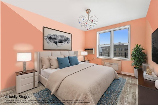 bedroom featuring a wall mounted air conditioner, baseboards, a notable chandelier, and wood finished floors