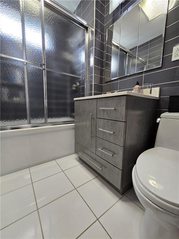 full bath featuring tile patterned flooring, toilet, bath / shower combo with glass door, tile walls, and vanity