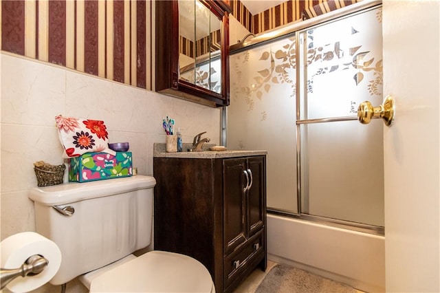 bathroom featuring toilet, vanity, combined bath / shower with glass door, and tile walls