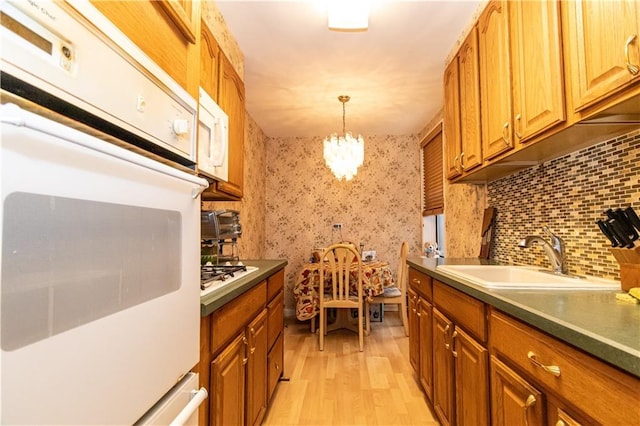 kitchen featuring light wood-style floors, an inviting chandelier, white appliances, a sink, and wallpapered walls