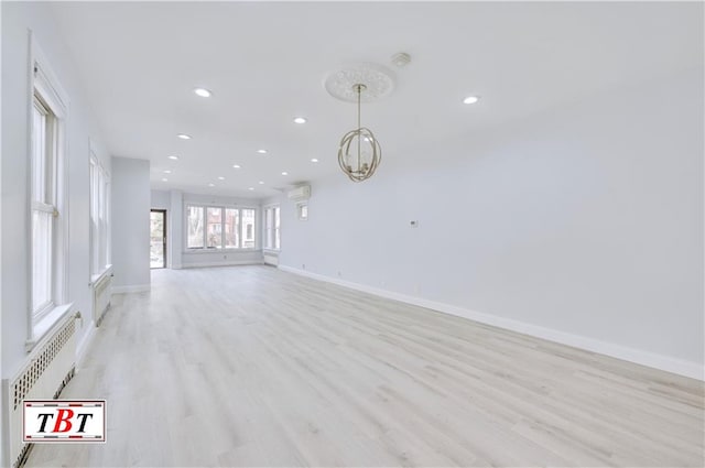 unfurnished living room with light wood-style floors, recessed lighting, baseboards, radiator, and a chandelier