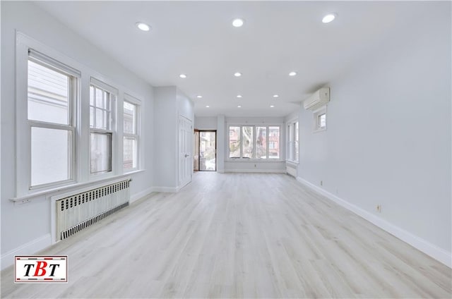 unfurnished living room featuring radiator, a wall unit AC, light wood-style floors, baseboards, and recessed lighting