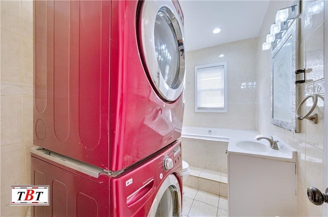laundry area featuring stacked washer / drying machine, light tile patterned floors, and tile walls
