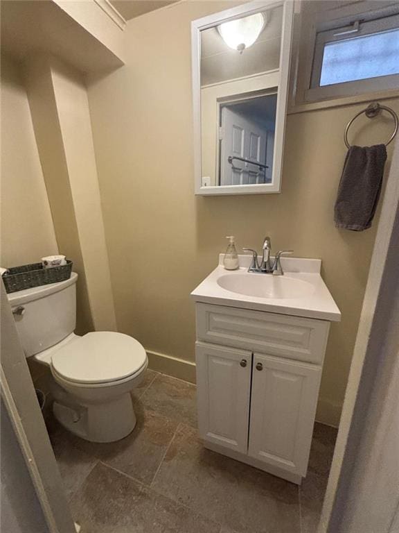 bathroom with stone finish floor, toilet, vanity, and baseboards