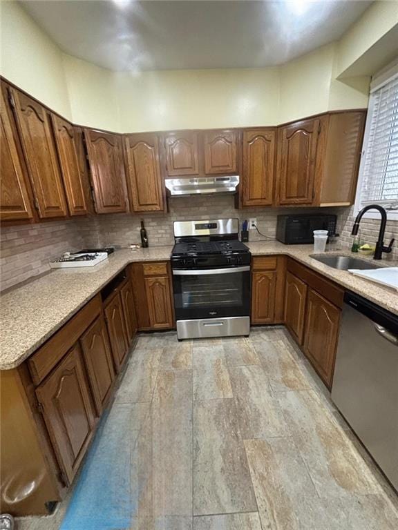 3883 Bedford Ave, Brooklyn, NY 11229 - kitchen with appliances with stainless steel finishes, under cabinet range hood, a sink, tasteful backsplash, and brown cabinetry