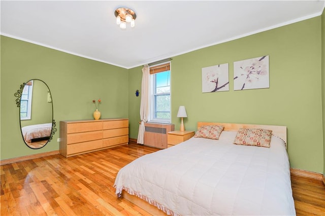 bedroom with radiator, ornamental molding, wood finished floors, and baseboards