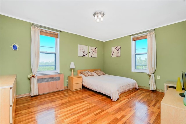 bedroom featuring multiple windows, light wood-style floors, radiator heating unit, ornamental molding, and baseboards